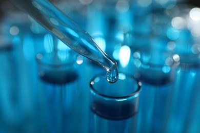 Photo of Dripping liquid into test tubes on blurred background, closeup