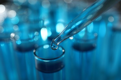 Photo of Dripping liquid into test tubes on blurred background, closeup