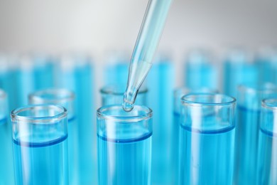 Photo of Dripping liquid into test tubes on light background, closeup