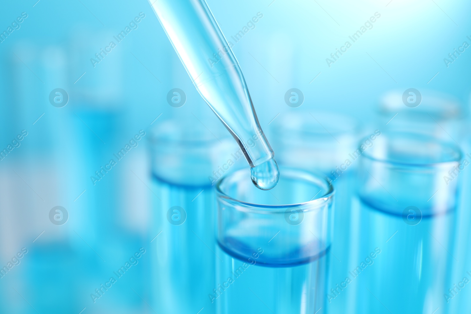 Photo of Dripping liquid into test tubes on blue background, closeup