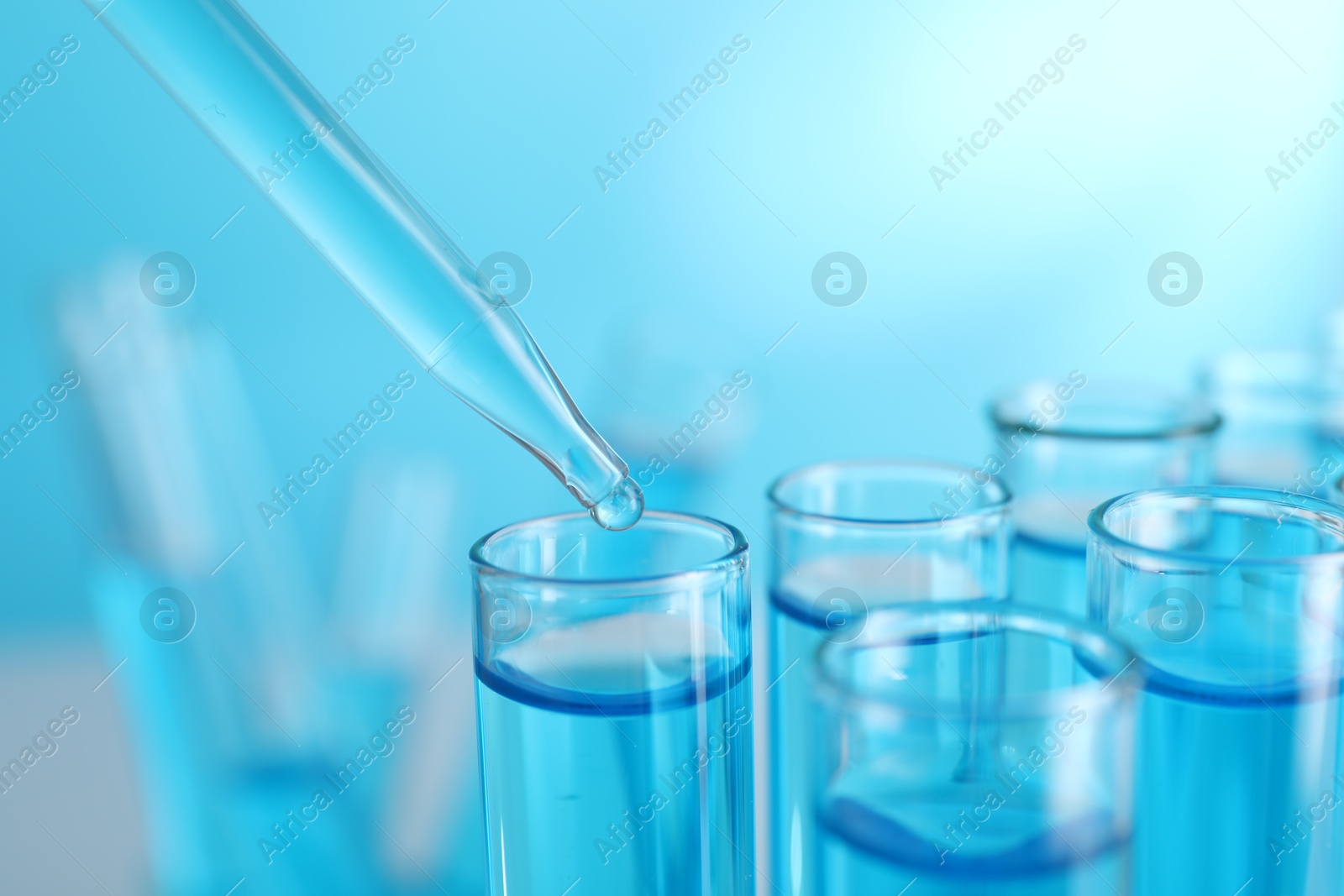 Photo of Dripping liquid into test tubes on blue background, closeup