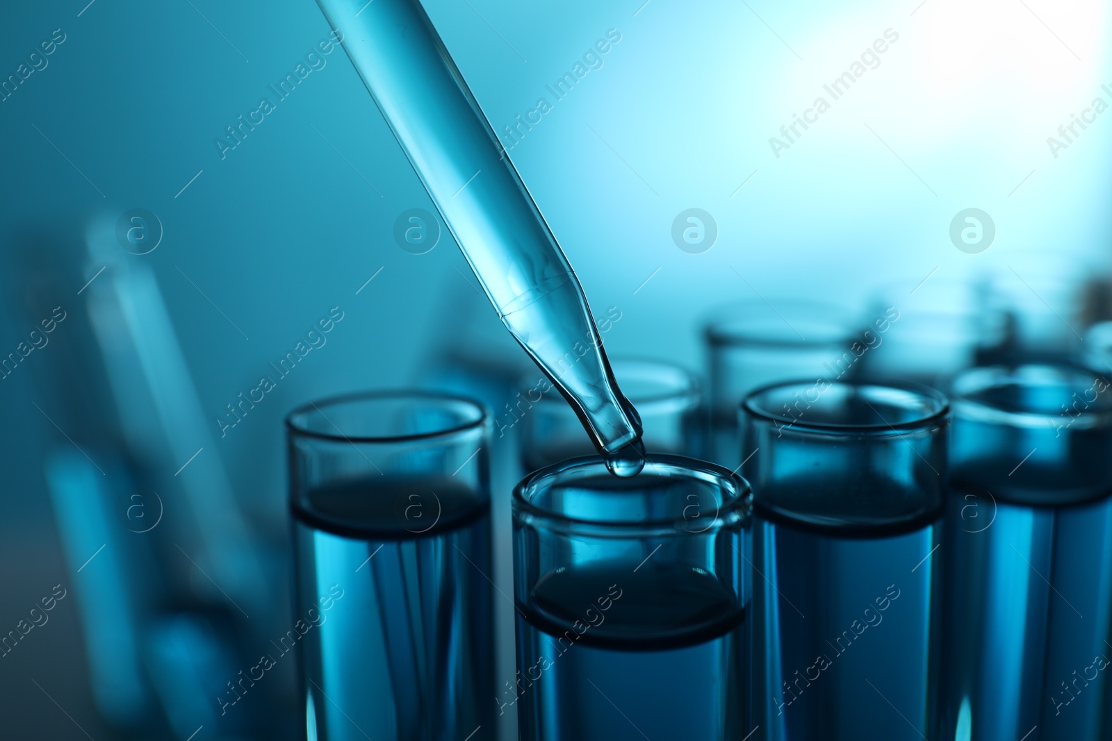 Photo of Dripping liquid into test tubes on blue background, closeup. Color toned effect