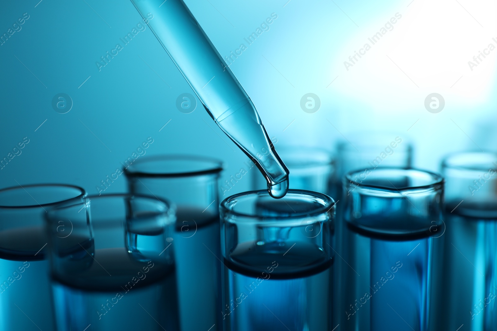 Photo of Dripping liquid into test tubes on blue background, closeup. Color toned effect