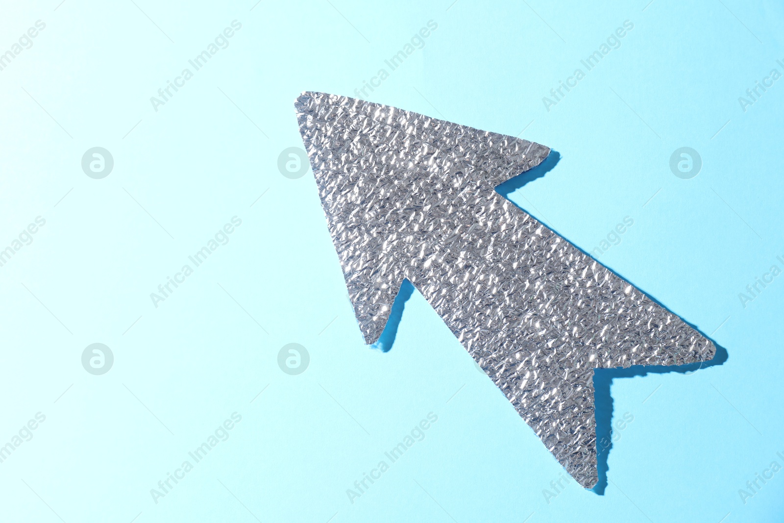 Photo of Silver tinfoil arrow on light blue background, top view. Space for text