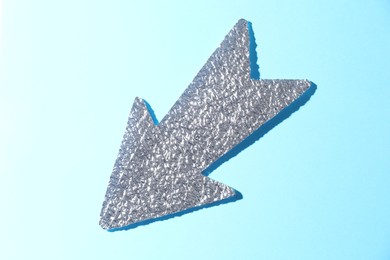 Photo of Silver tinfoil arrow on light blue background, top view