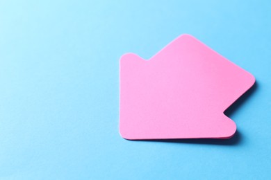 Photo of One pink paper arrow on light blue background, closeup. Space for text