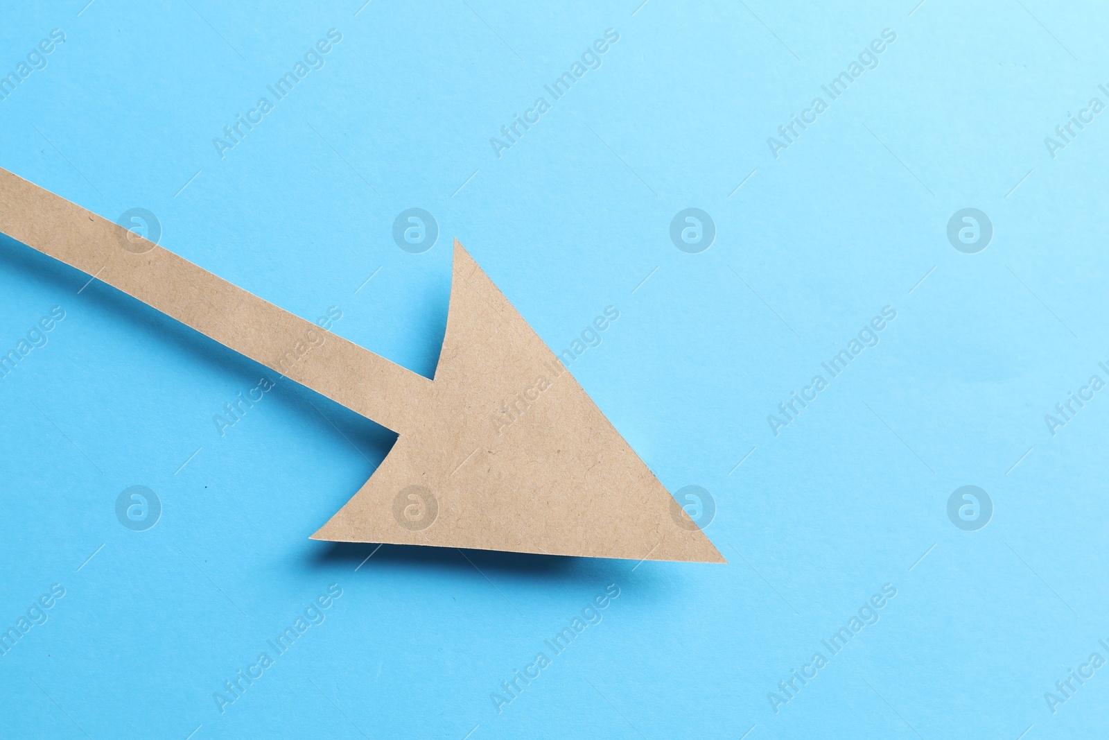 Photo of One kraft paper arrow on light blue background, top view. Space for text