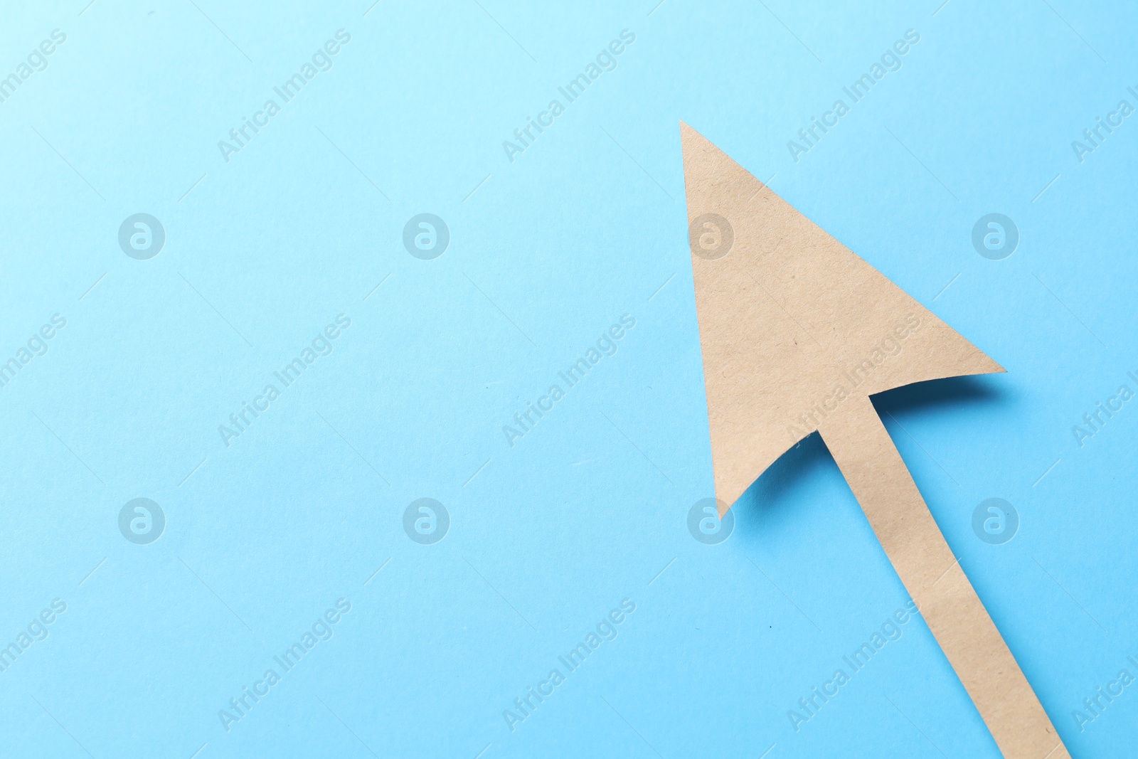 Photo of One kraft paper arrow on light blue background, top view. Space for text