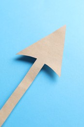 Photo of One kraft paper arrow on light blue background, top view