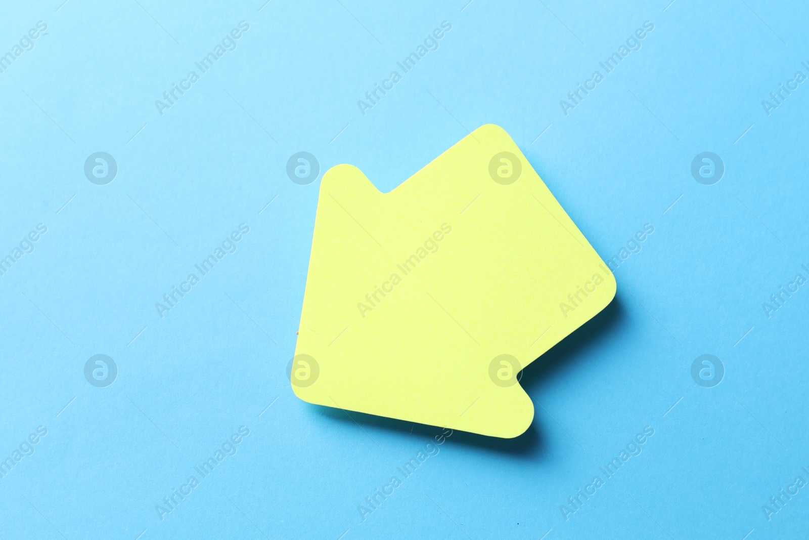 Photo of One yellow paper arrow on light blue background, top view