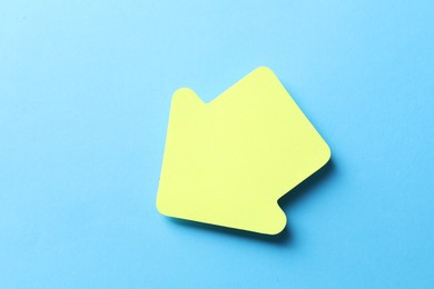 Photo of One yellow paper arrow on light blue background, top view