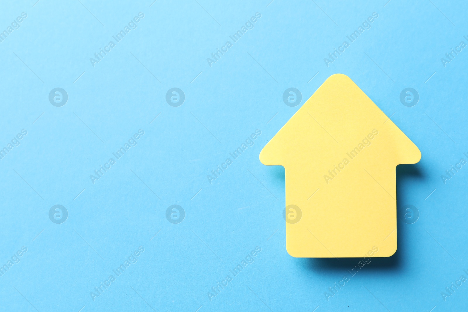 Photo of One yellow paper arrow on light blue background, top view. Space for text