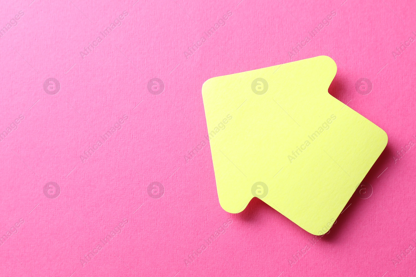 Photo of One yellow paper arrow on pink background, top view. Space for text