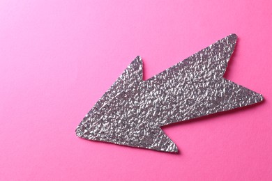 Photo of Silver tinfoil arrow on pink background, top view. Space for text