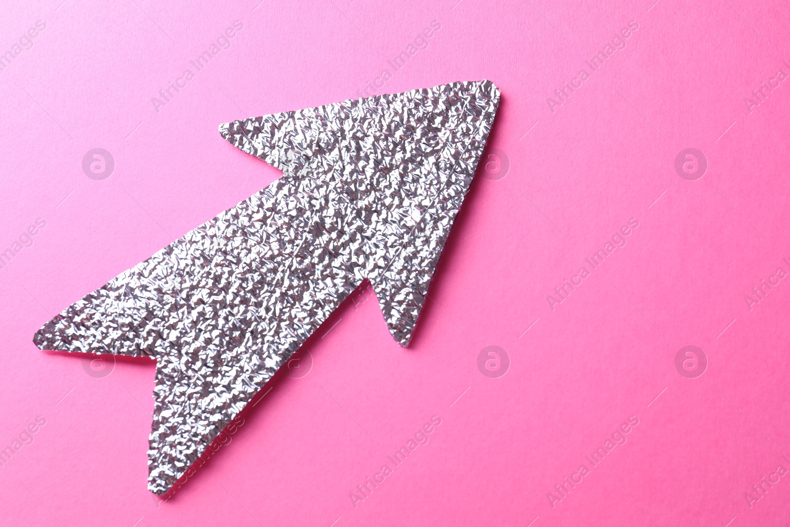 Photo of Silver tinfoil arrow on pink background, top view. Space for text