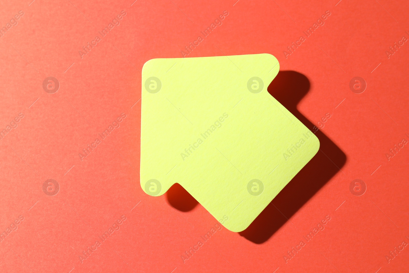 Photo of One yellow paper arrow on red background, top view