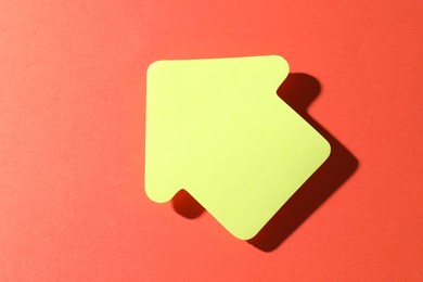 Photo of One yellow paper arrow on red background, top view