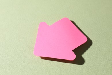 Photo of One pink paper arrow on light green background