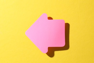 Photo of One pink paper arrow on yellow background, top view