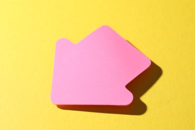 Photo of One pink paper arrow on yellow background, closeup