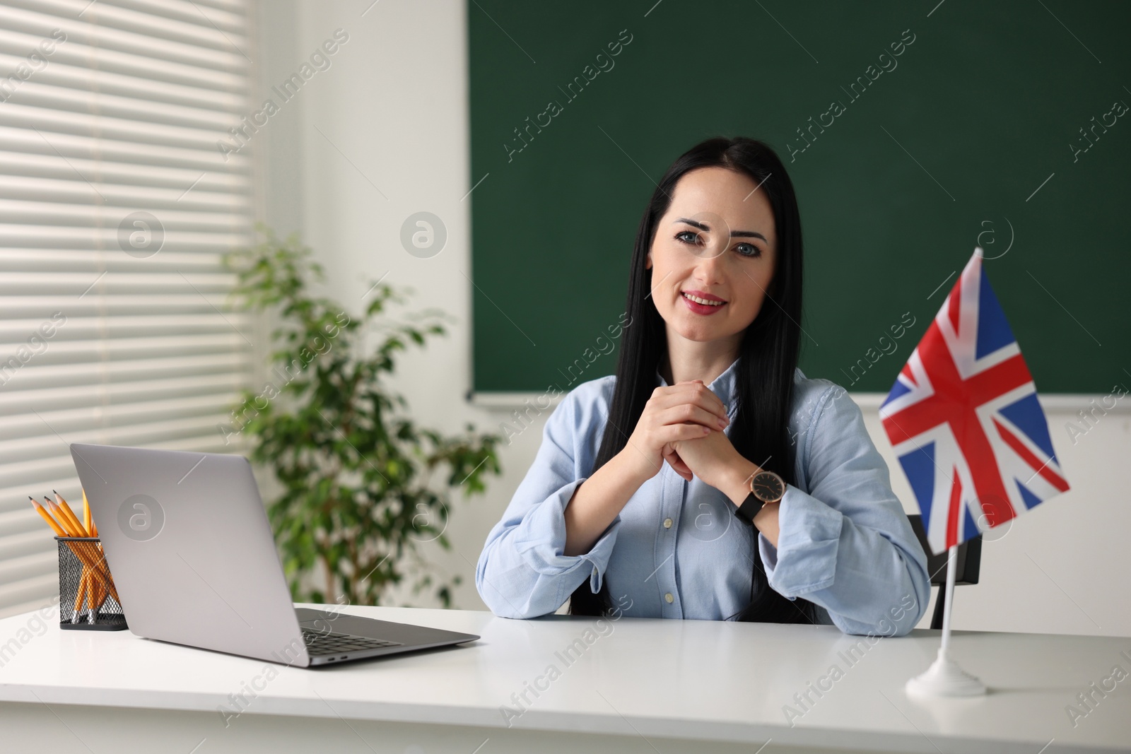 Photo of English teacher with laptop at desk in classroom. Space for text