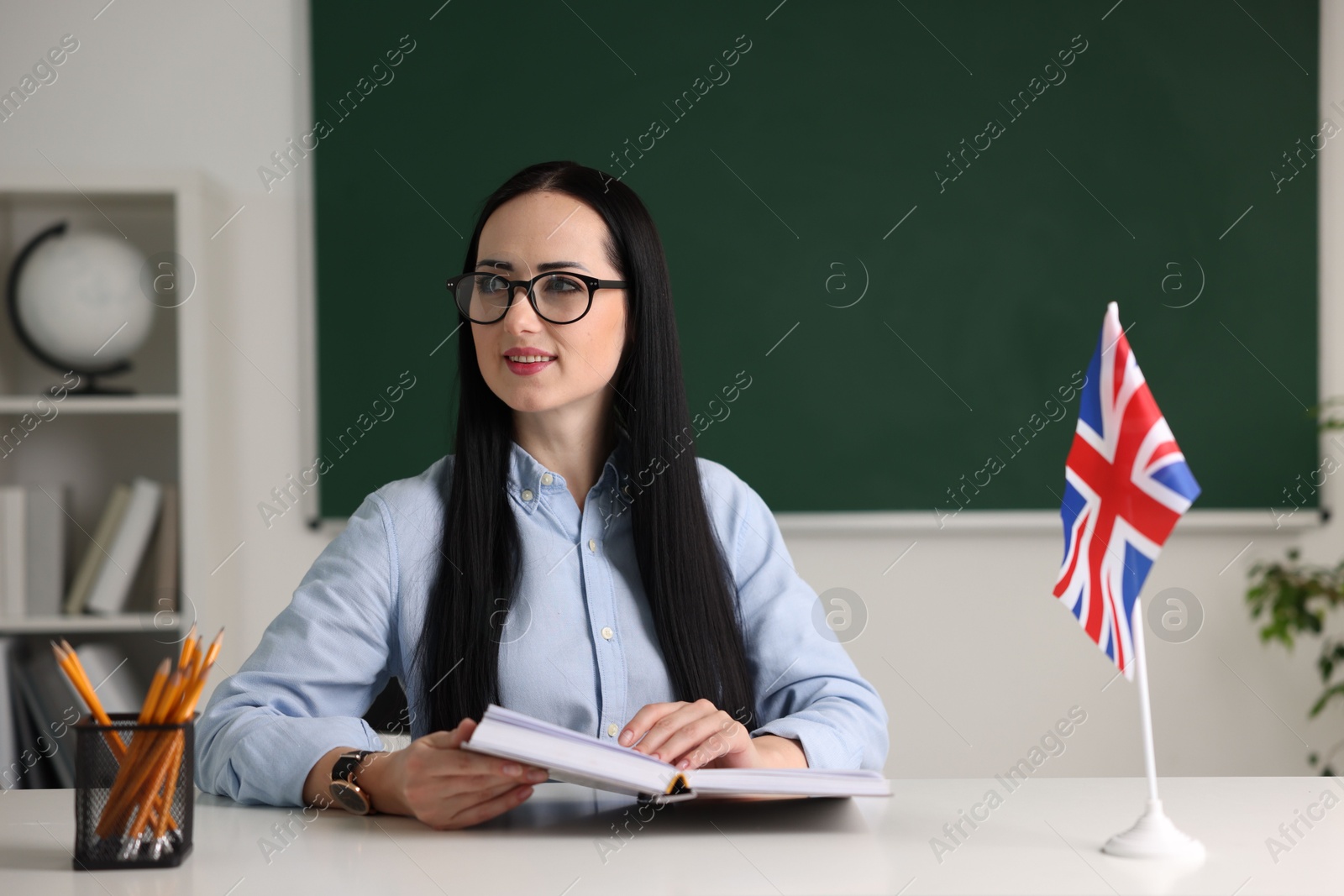 Photo of English teacher with book at desk in classroom