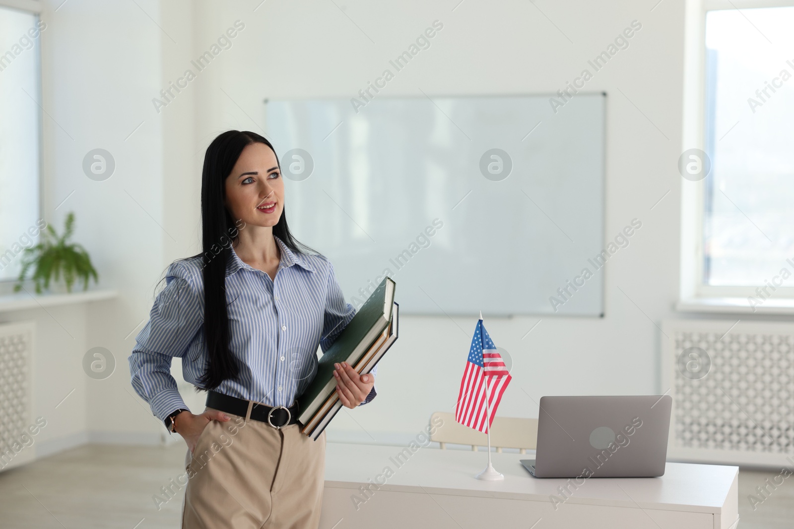 Photo of English teacher with books at desk in classroom. Space for text