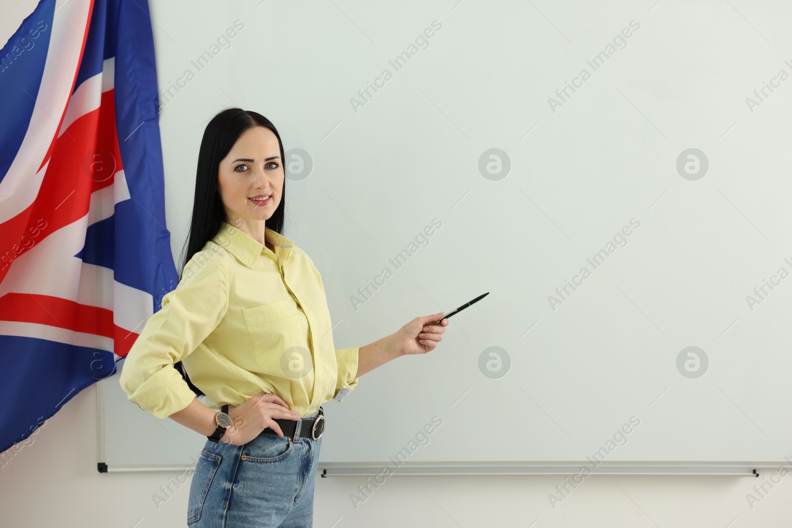 Photo of English teacher explaining something near whiteboard in classroom. Space for text