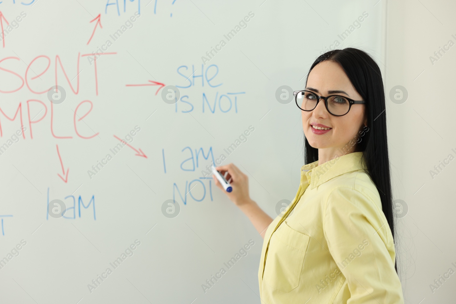 Photo of English teacher explaining Present Simple tense at whiteboard in classroom