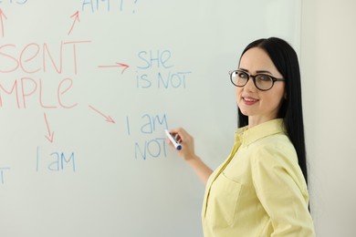 Photo of English teacher explaining Present Simple tense at whiteboard in classroom