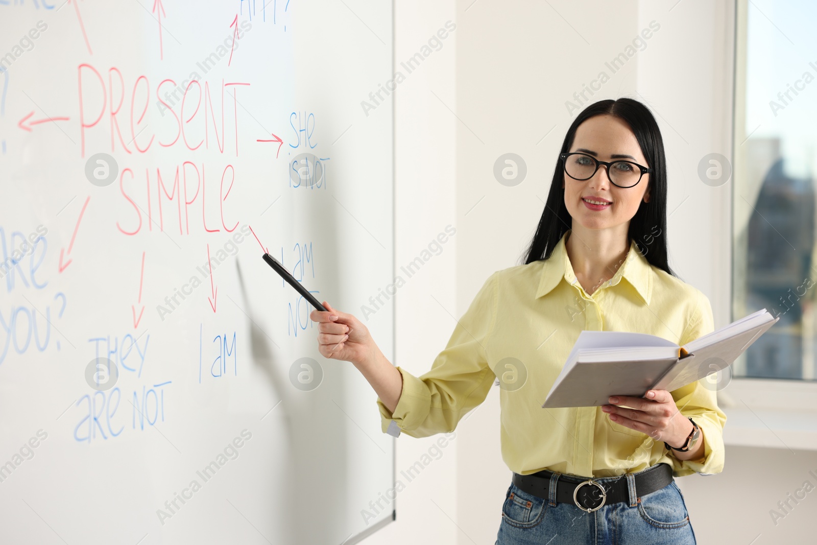 Photo of English teacher explaining Present Simple tense at whiteboard in classroom