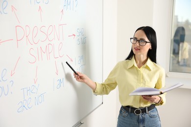 Photo of English teacher explaining Present Simple tense at whiteboard in classroom