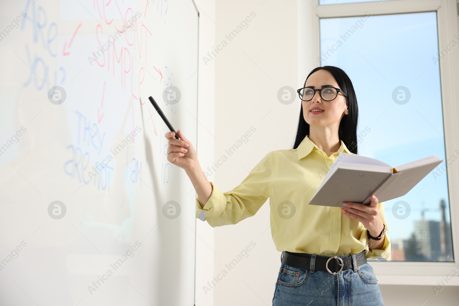 Photo of English teacher explaining Present Simple tense at whiteboard in classroom