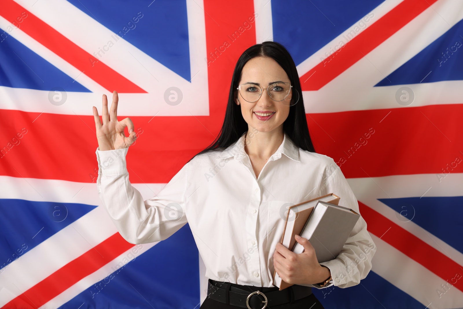 Photo of English teacher with books showing ok gesture against UK flag