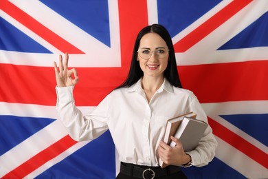 Photo of English teacher with books showing ok gesture against UK flag