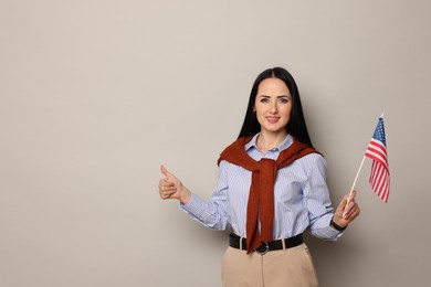 Photo of English teacher with American flag showing thumbs up on light grey background. Space for text