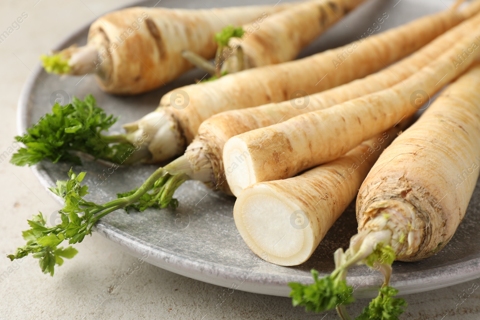 Photo of Whole and cut fresh parsley roots on grey table, closeup