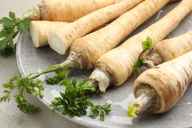 Photo of Whole and cut fresh parsley roots on table, closeup