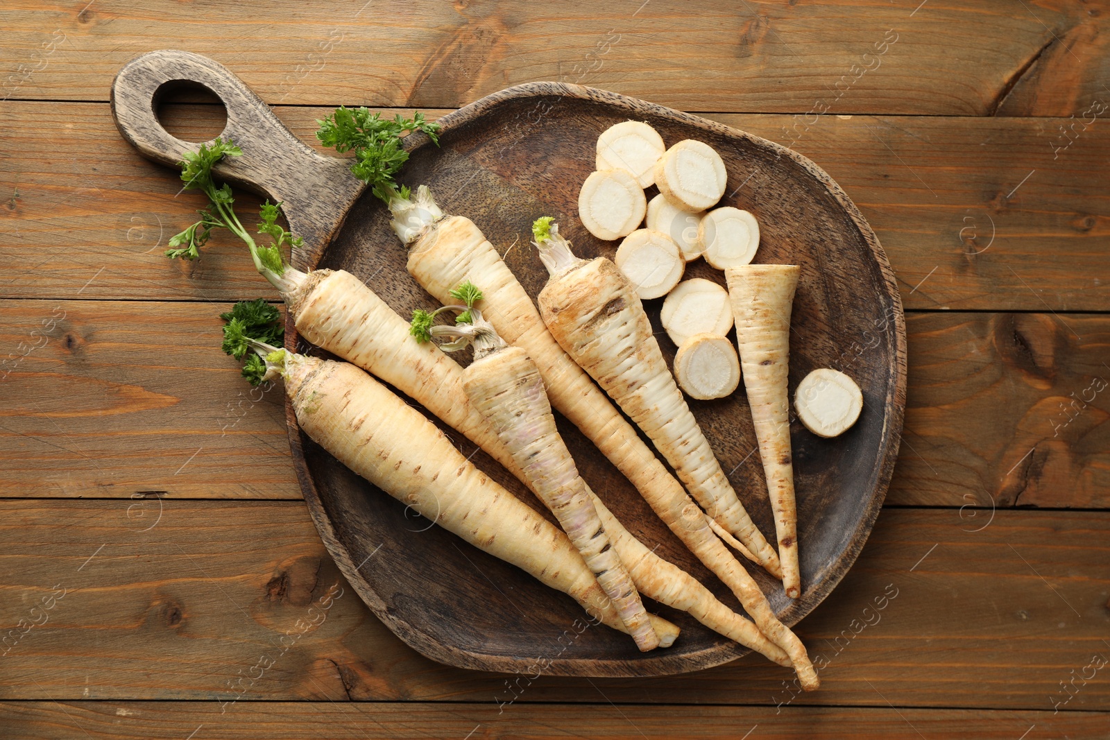 Photo of Whole and cut fresh parsley roots on wooden table, top view