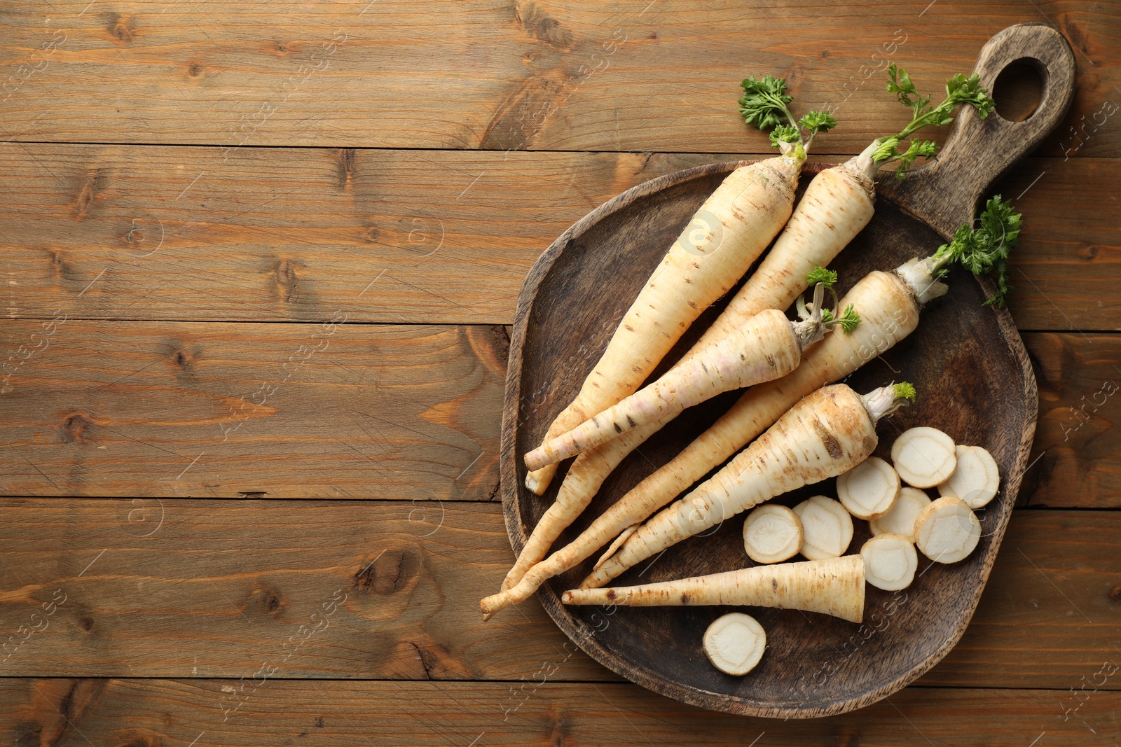 Photo of Whole and cut fresh parsley roots on wooden table, top view. Space for text