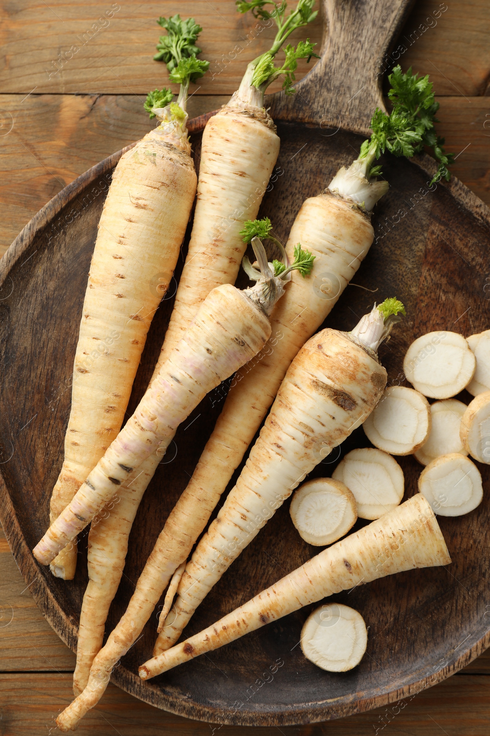 Photo of Whole and cut fresh parsley roots on wooden table, top view