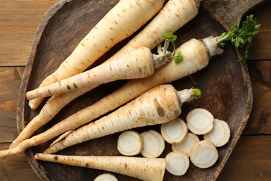 Photo of Whole and cut fresh parsley roots on wooden table, top view