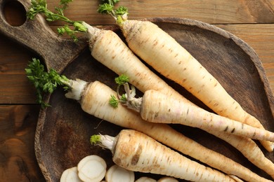 Photo of Whole and cut fresh parsley roots on wooden table, top view