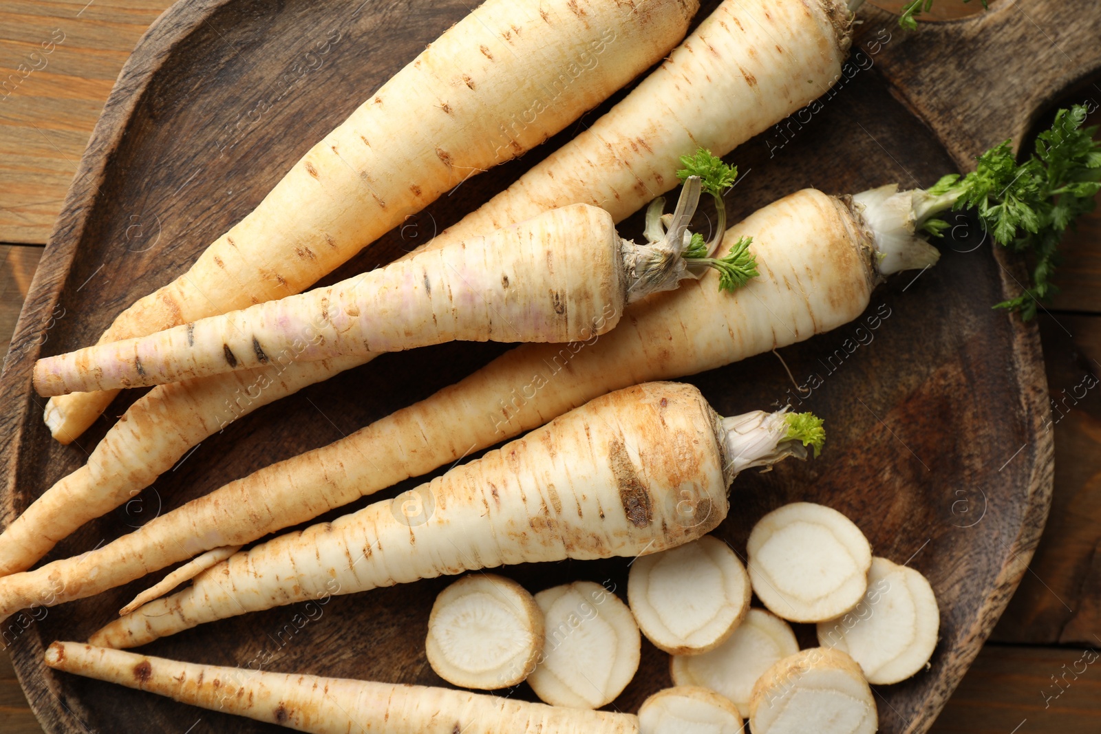 Photo of Whole and cut fresh parsley roots on wooden table, top view