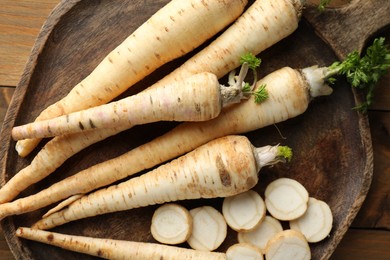 Photo of Whole and cut fresh parsley roots on wooden table, top view