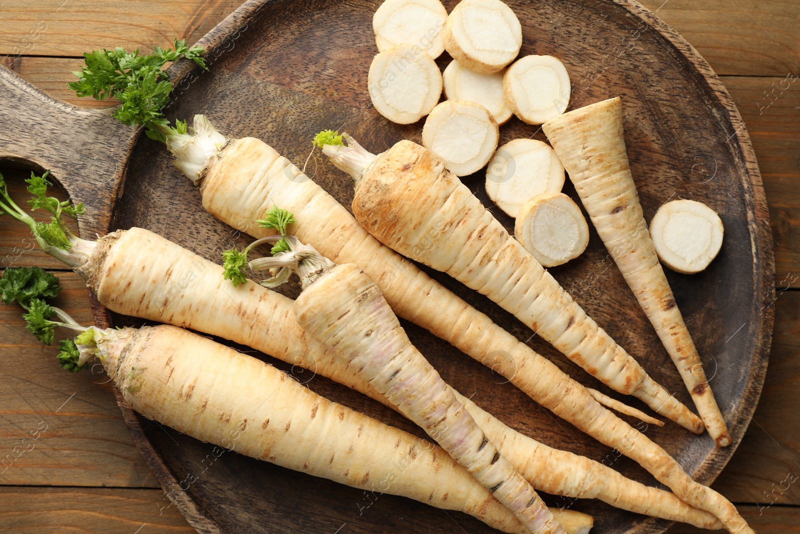 Photo of Whole and cut fresh parsley roots on wooden table, top view