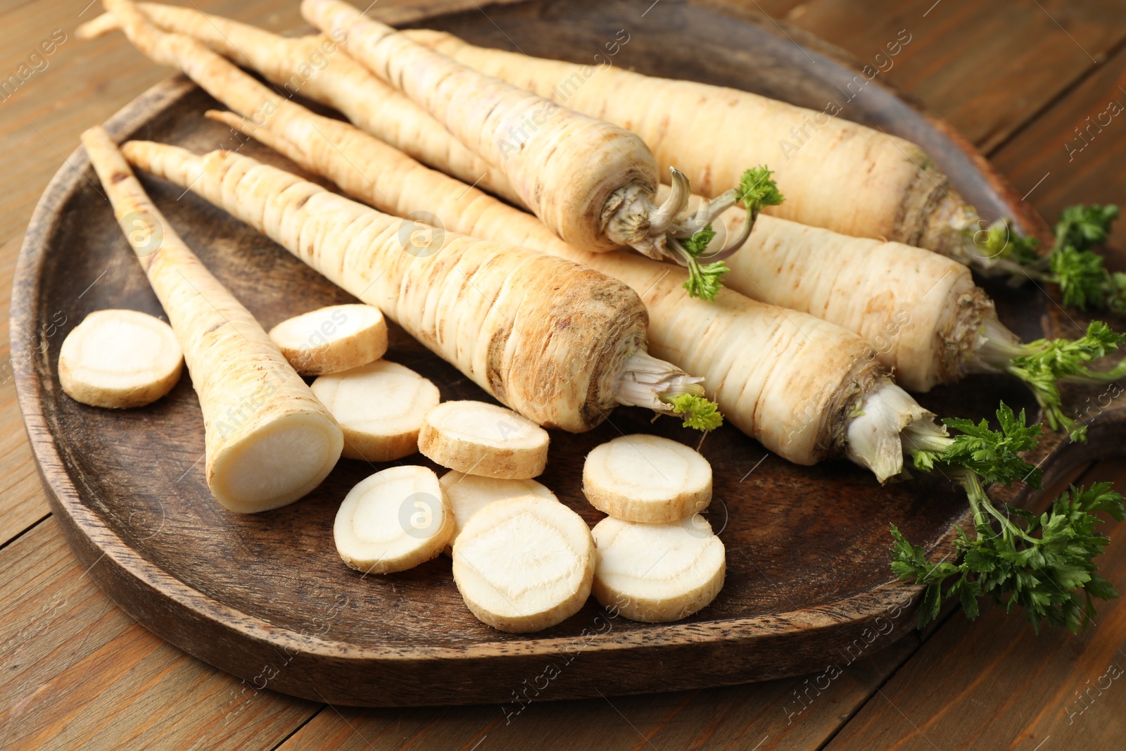 Photo of Whole and cut fresh parsley roots on wooden table, closeup