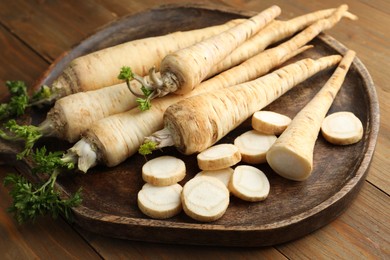 Photo of Whole and cut fresh parsley roots on wooden table, closeup