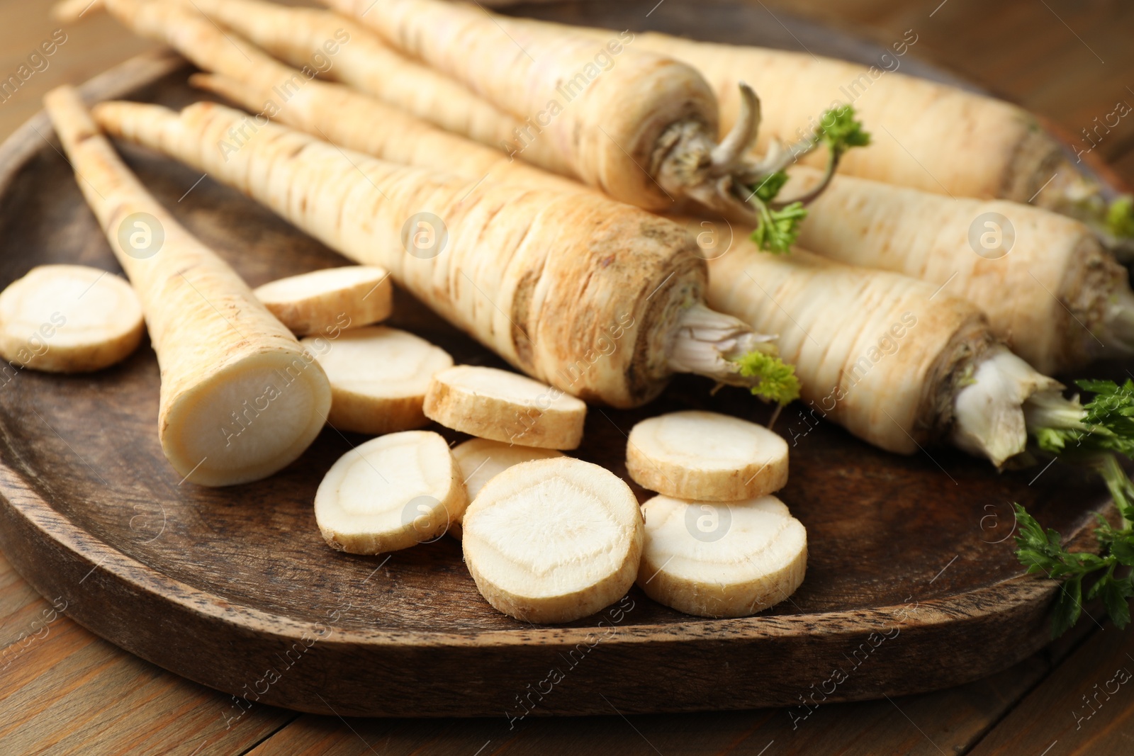 Photo of Whole and cut fresh parsley roots on wooden table, closeup