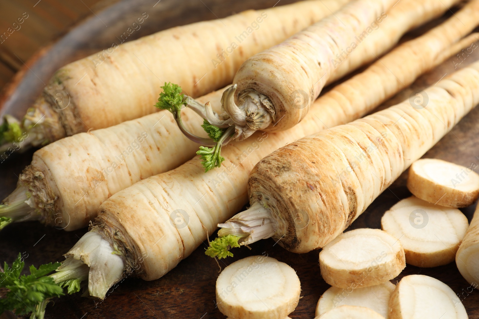 Photo of Whole and cut fresh parsley roots on table, closeup